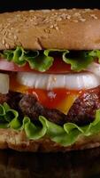 Fresh appetizing Beef Burger is rotating. Delicious burger with fresh iceberg cabbage, onions, tomatoes and grilled steak. Rotating - fast food, Close-up, vertical footage video