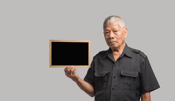 An elderly Asian man holding a mini blackboard and looking at the camera with a smile while standing on a gray background photo