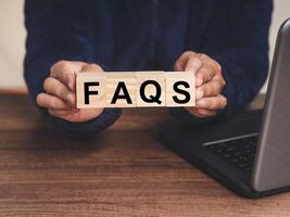 Close-up of hands holding wooden cubes with the letter FAQS while sitting at the table photo