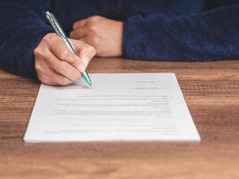 Close-up of businessman in a sweater signing a lease contract or agreement while sitting at the table photo
