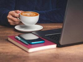Close-up of hand holding a cup of coffee while sitting at the table photo