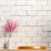 3D A golden platform is shown on a light surface, with a vase of pink flowers to the left. The backdrop is a white brick wall. The scene is minimalist and has a rustic, natural feel. photo