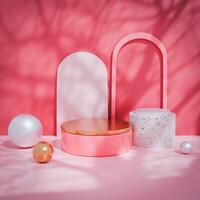 3D Pink circular platform with gold top beside white-gray cylinder platform, white and gold spheres arranged around. Light pink wall with arches. Modern, playful design, strong color palette. photo