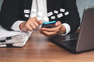 Close-up of businesswoman using a smartphone receives a new message with email icons while sitting at the table photo