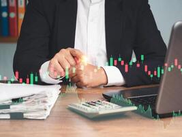 Businessman in a suit pointing to graph stock on a virtual screen while sitting at the table photo