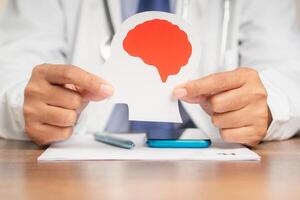 Doctor in a uniform holding a brain symbol made from paper while sitting at the table photo