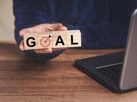 Close-up of hand holding wooden cubes with letters GOAL and dartboard icon while sitting at the table photo