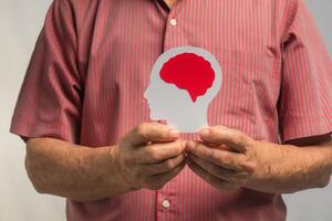 Close-up of hands senior man holding a brain symbol while standing on a gray background photo