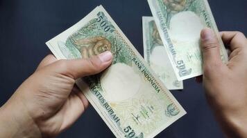 A man shows some old rupiah money with a nominal value of 500 rupiah. Isolated on black background, close up view video