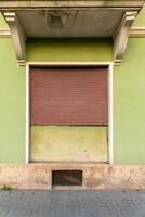 Abandoned storefront with a closed shutter in a vibrant green facade in a quiet urban setting photo