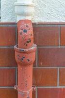 Rusty water pipe with chipped paint against tiled wall in urban setting under evening light photo