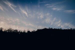 Dramatic twilight sky over silhouetted trees on a serene hillside during the evening hours photo