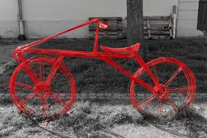 Creative red wire bicycle sculpture displayed on the sidewalk next to a grassy area in an urban setting photo