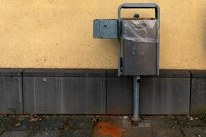 Metal waste container attached to a wall in an urban setting during daylight hours photo