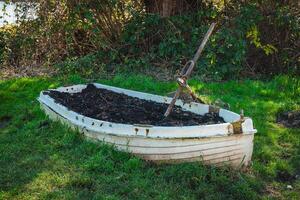 Old abandoned boat sits on green grass, surrounded by shrubs and trees in a tranquil rural setting photo