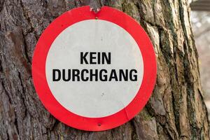 Sign prohibiting with the german words no passage entry stands on a tree in a forest, expressing a clear message about restricted access under gloomy weather photo