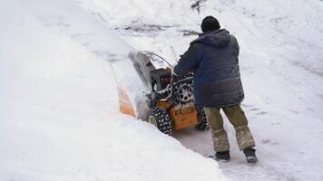 Man using snowblower to remove snow after winter cyclone. He is assisted by thrower on winter road. Man is with snow blower on winter road after snow storm. Handheld. Kamchatka, Russia - Dec 28, 2023 video