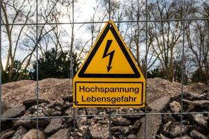Caution sign warning of high voltage danger with the german words high voltage life threatening near a construction site during cloudy weather photo