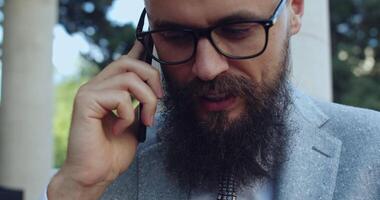 A confident businessman is actively engaging in a mobile conversation in a casual city setting video