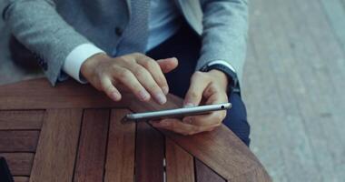 A professional is actively using a smartphone while seated at an outdoor table in a public setting video
