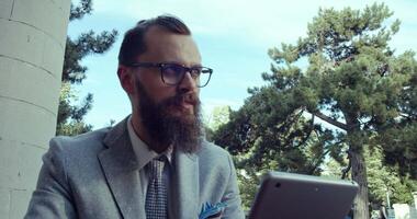 A Businessman Dressed in a Stylish Suit is Using a Tablet Outdoors While Enjoying Nature video