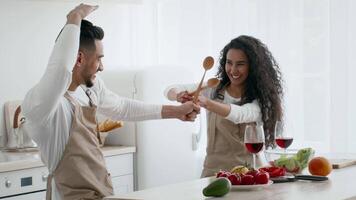 A happy couple engages in a playful cooking activity in a bright, modern kitchen. They use wooden spoons and laugh while preparing a colorful array of fresh ingredients together. video