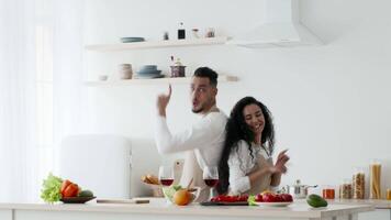 A Middle Eastern couple enjoys cooking together in a bright kitchen. They are surrounded by fresh vegetables and beverages, celebrating their culinary skills with joyful movements. video