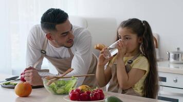 A father and his daughter are enjoying quality time in their bright kitchen. They are preparing a nutritious salad while sharing a moment of laughter and joy. video