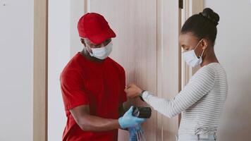A courier delivers a package to a woman's apartment. Both are wearing masks, emphasizing safety during the delivery process. The interaction takes place indoors, in a modern setting. video