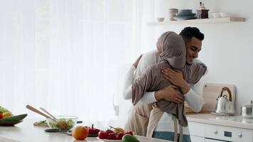A joyful couple shares a loving hug in their bright kitchen. The space is adorned with fresh fruits and vegetables, creating a warm and inviting atmosphere for cooking together. video
