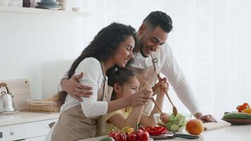 A family enjoys quality time preparing a healthy meal in a modern kitchen. The parents guide their child as they chop vegetables and mix ingredients, fostering togetherness. video