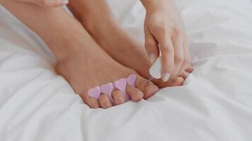 A young Middle Eastern woman enjoys a moment of self-care at home, applying nail polish to her toes while using heart-shaped toe separators for better grooming. video