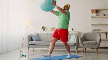 A chubby millennial man engages in a workout routine at home, using a stability ball for his fitness session. He wears comfortable athletic clothing and focuses on his exercise. video