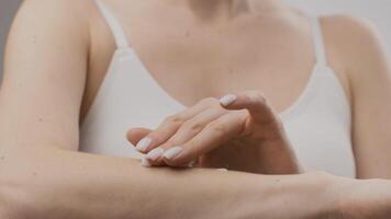 A young woman demonstrates a skin care routine, applying lotion with careful attention. The focus is on her arm, showcasing effective pampering practices in a minimalistic setting. video