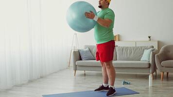A man is engaged in a workout routine at home using an exercise ball. He wears athletic clothing and focuses on his fitness journey. The bright and airy space enhances the motivating atmosphere. video