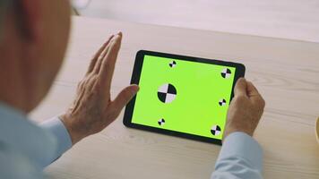An elderly man in his 60s enjoys a leisurely afternoon at home, engaging with a tablet displaying colorful graphics. He appears focused and relaxed during his retirement. video