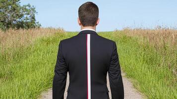 Man in Black Suit Walking on Grass Path Towards Bright Horizon photo