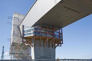 A close-up view of a bridge under construction, showcasing the concrete support structure and scaffolding. The sky is clear with a few clouds, highlighting the construction work. photo