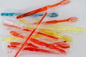A collection of colorful toothbrushes in plastic packaging, featuring red, yellow, and blue colors, arranged haphazardly on a white surface. photo