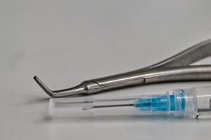 A close-up of dental tools including a curved dental instrument and a syringe with a needle, placed on a light surface. photo