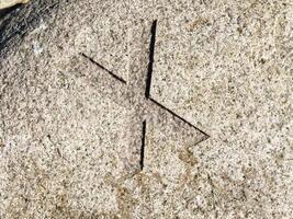 A close-up view of a carved stone featuring a cross-like symbol etched into its surface. The texture of the stone is rough and natural, with visible grains and colors. photo