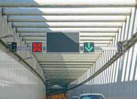 Traffic lights indicating lane usage in a tunnel, with a red X signal and a green downward arrow. The tunnel has a modern design with overhead beams and a clear road ahead. photo