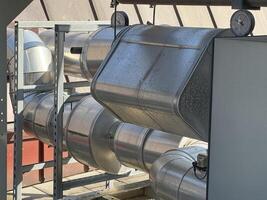 A close-up view of large metallic ducts and pipes, showcasing their shiny surfaces and industrial design. The setting appears to be an outdoor facility with sunlight reflecting off the metal. photo