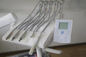 A close-up view of a dental chair control panel with multiple hoses and a digital display, set in a modern dental clinic environment. photo
