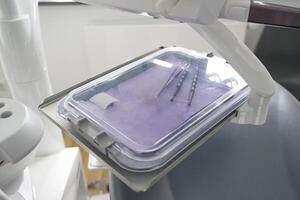 A close-up view of dental instruments placed on a sterile tray in a dental clinic. The tray is covered with a transparent lid, showcasing the tools used for dental procedures. photo
