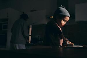 Focused little boy cutting banana on board near anonymous mother photo