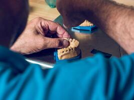 Crop dental technician inserting teeth into denture photo