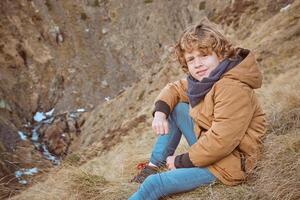Smiling boy in warm clothes sitting on grassy hill photo