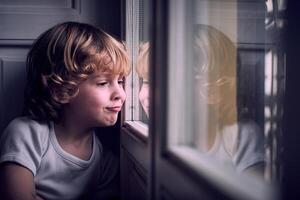 Cute child making face and looking through window at home photo