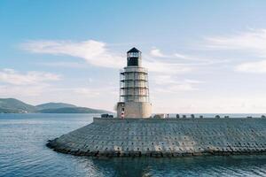 Lighthouse on a breakwater in the sea against the backdrop of a mountain range photo